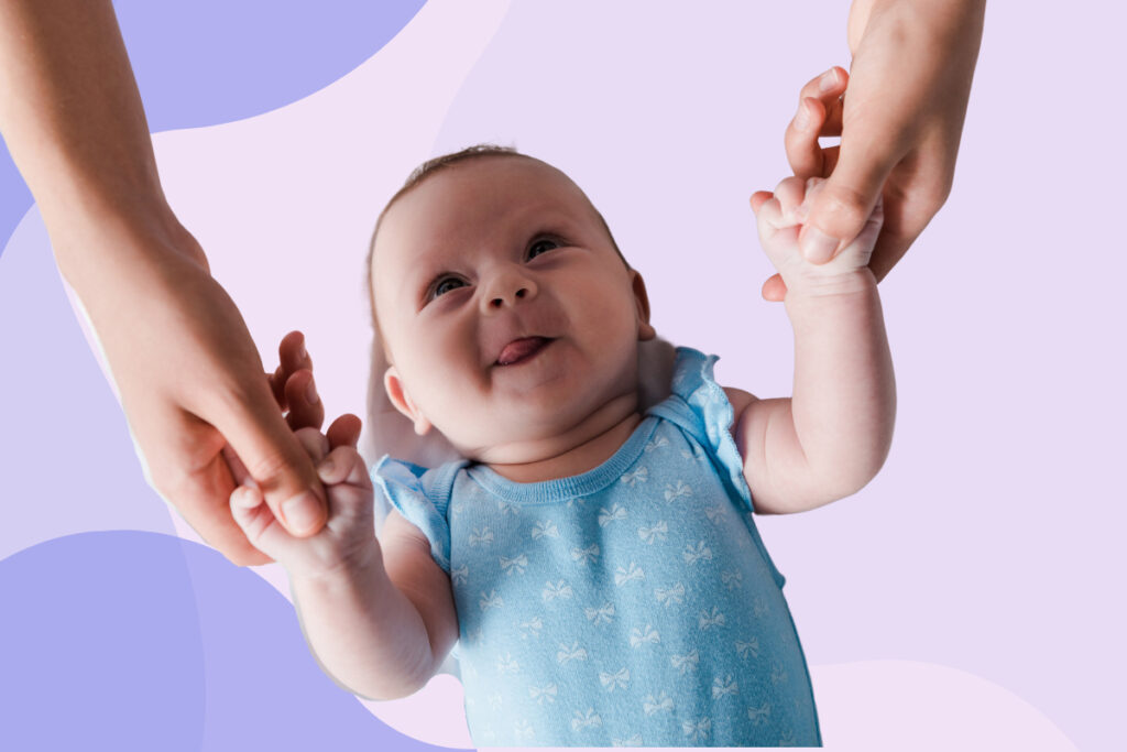 A smiling baby looks up at someone playing with their hands.