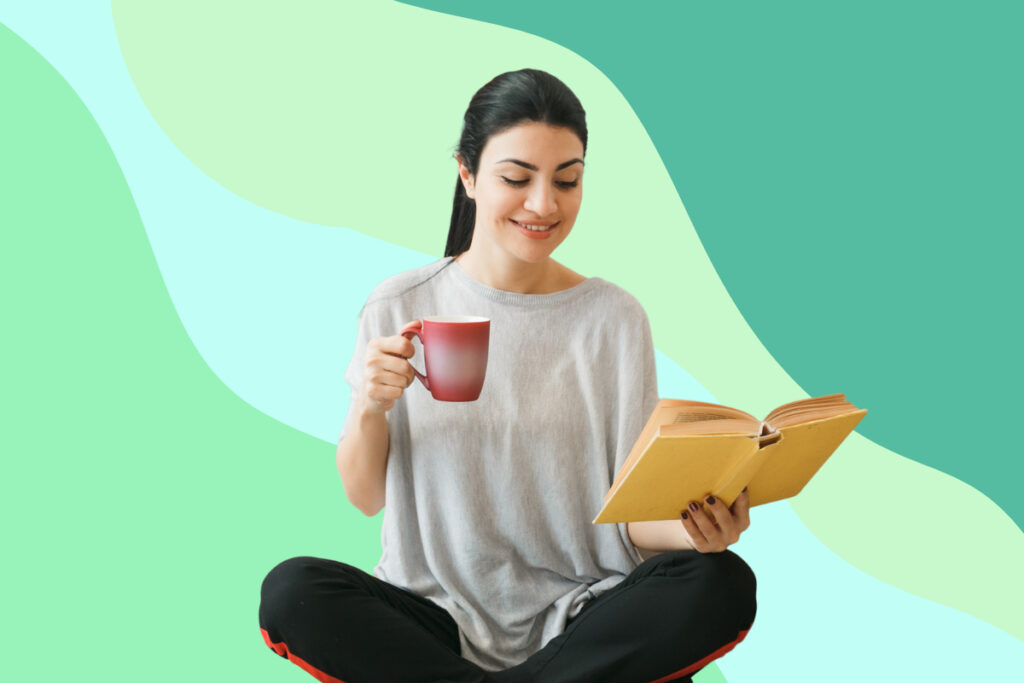 woman smiling while holding a cup and reading a book
