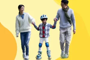 A pair of parents hold their son's hand on either side as he rollerskates.