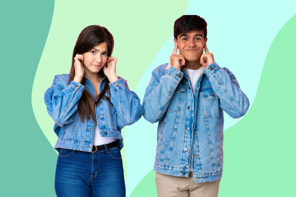 A teenage boy and girl stand pulling faces with their fingers in their ears.