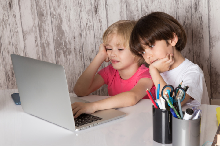 boy and girl stare at laptop appearing bored. how do you motivate children in distance learning is the question