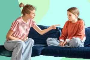A mother points and scolds a young girl sitting on the couch.