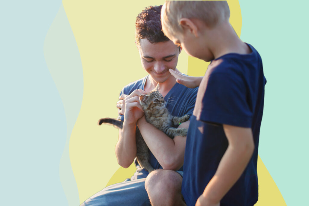 A man holding a kitten that a young boy is petting.