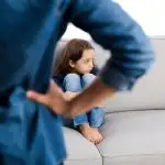 girl sits on couch in front of a strict parent