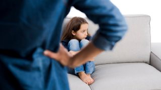 girl sits on couch in front of a strict parent