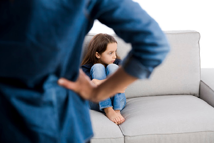 girl sits on couch in front of a strict father, strict parents examples