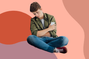 depressed teenage boy sits on floor holding a cellphone