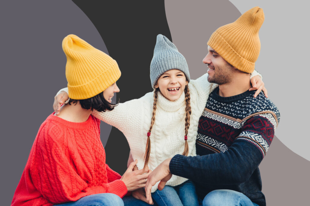 A mother, father, and daughter wearing matching beanies and embracing.
