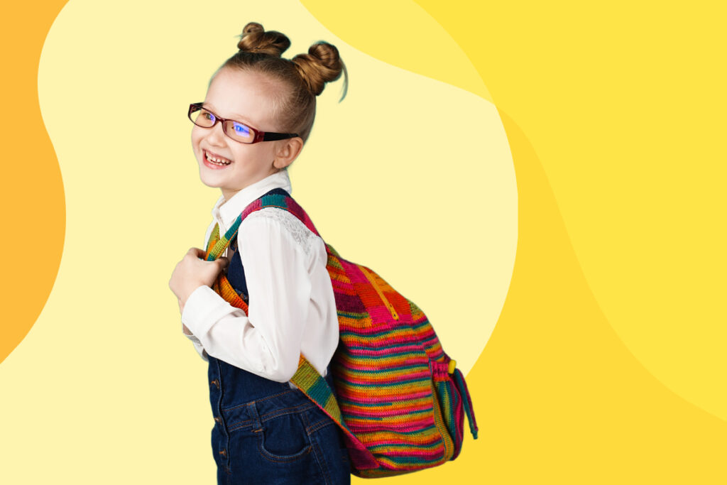 A grinning young girl carrying her school bag on her back.