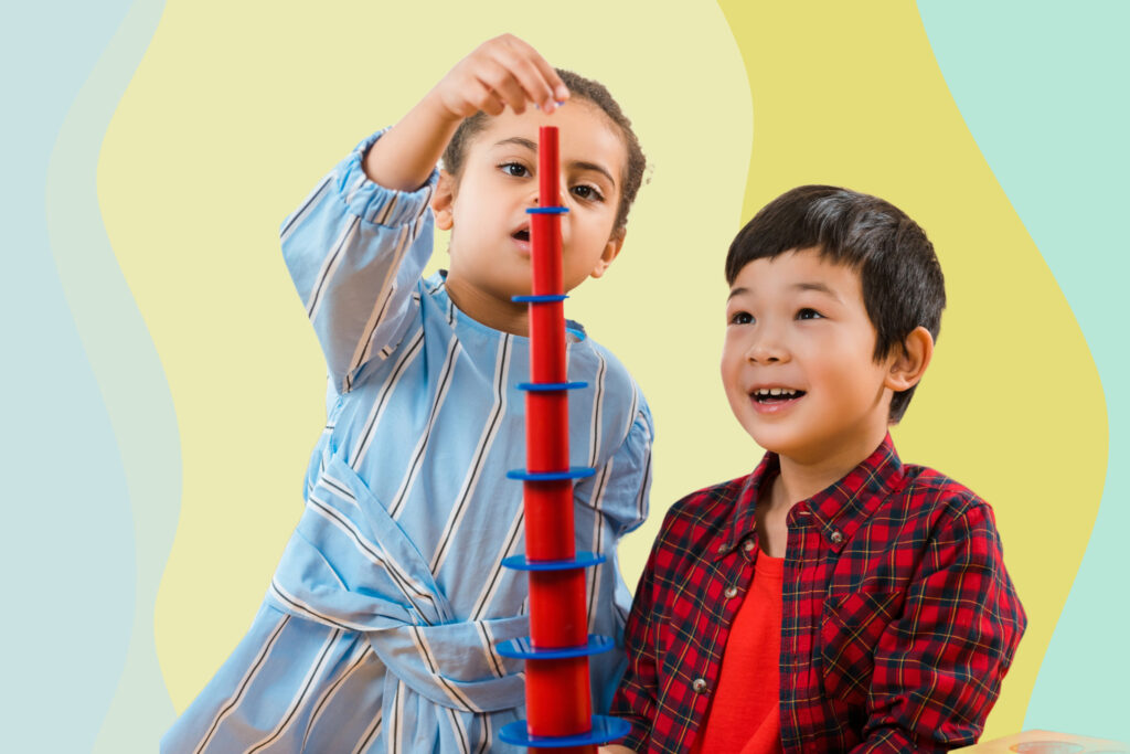 Two pre-school children build a plastic tower.